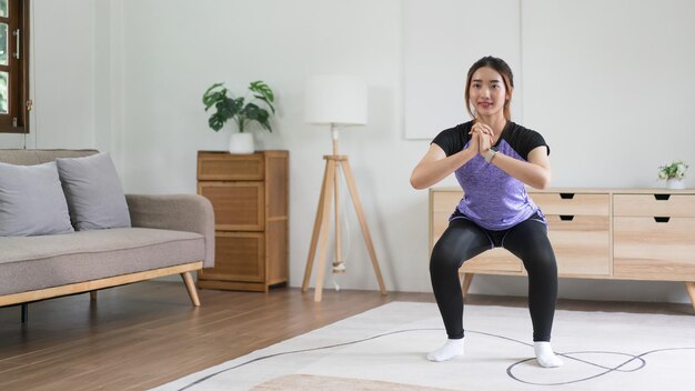 Młoda azjatycka kobieta robi ćwiczenia z treningiem w kucki na podłodze dla zdrowego stylu życia w domu