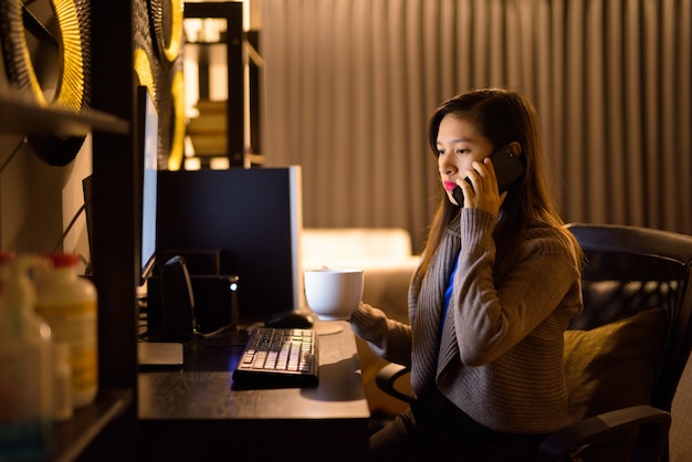 Młoda azjatycka kobieta rozmawia przez telefon podczas pracy w domu późno w nocy