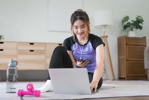 Młoda azjatycka kobieta słuchająca muzyki i oglądająca filmy fitness do przygotowania do ćwiczeń w domu