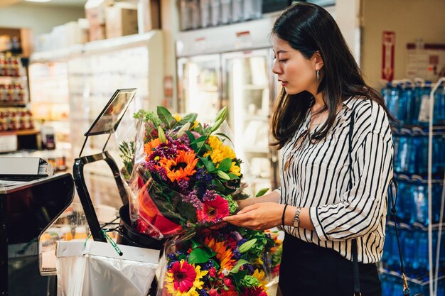 Młoda azjatycka kobieta trzyma piękny świeży kwiat kolorowe kwiaty w supermarkecie. Koncepcja ludzie konsumpcjonizmu zakupy. elegancka dama miłość rośliny kwiatowe hobby zakup do dekoracji mieszkania.