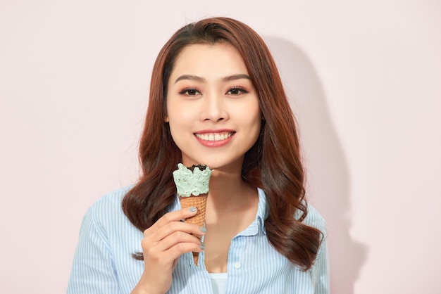 Młoda azjatycka kobieta trzyma smaczne lody, stoi na jasnoróżowym tle