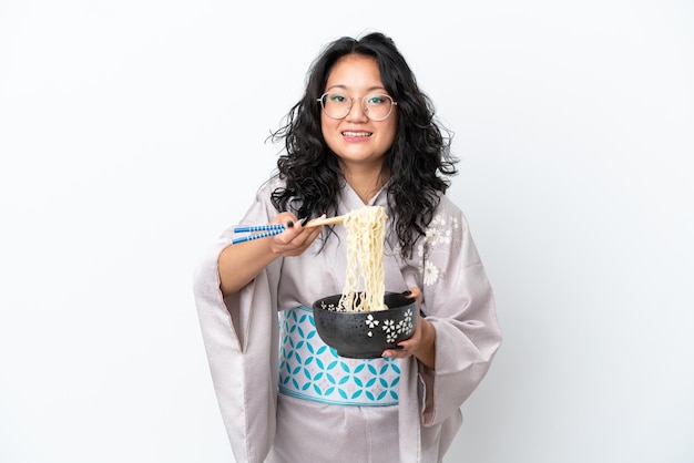 Młoda azjatycka kobieta ubrana w kimono na białym tle trzymająca miskę makaronu pałeczkami i oferująca ją