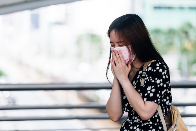 Zdjęcie młoda azjatycka kobieta ubrana w maskę i kichająca na ulicy