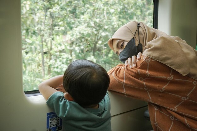Młoda azjatycka kobieta w hidżabie i jej syn rozmawiają i patrzą przez okno w pociągu