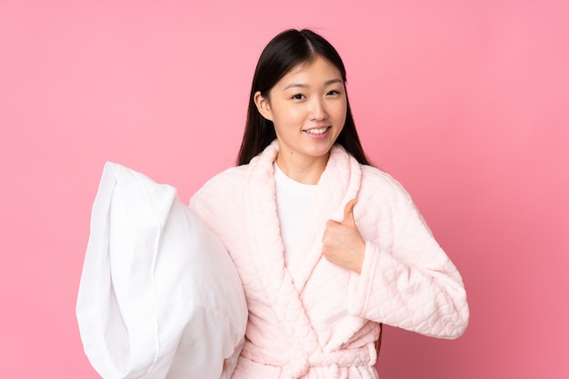 Młoda Azjatycka Kobieta W Piżamie Na Różowej ścianie Z Kciukami Do Góry, Ponieważ Stało Się Coś Dobrego