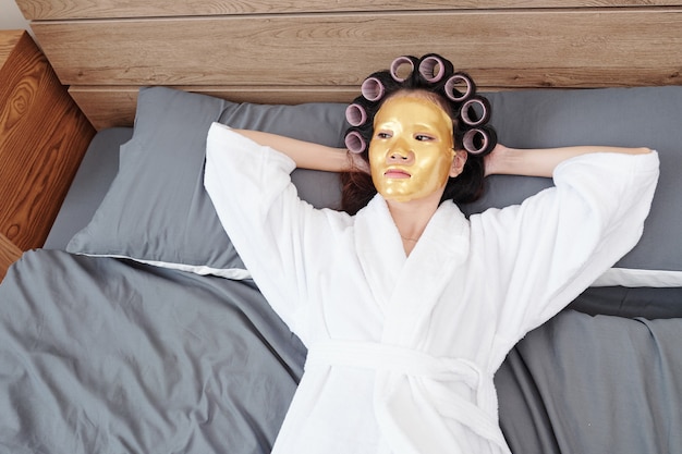 Młoda Azjatycka Kobieta W Szlafroku Odpoczywa Na łóżku Po Wzięciu Prysznica Z Silikonową Maską I Cieszy Się Swoim Spa I Dniem Urody