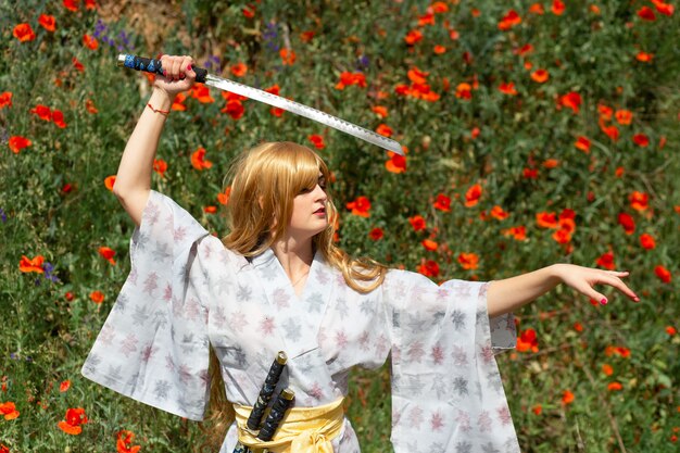 Młoda azjatycka kobieta w tradycyjnym kimonie trenuje techniki walki mieczem katana na wzgórzach z czerwonymi makami, samurajska wojowniczka