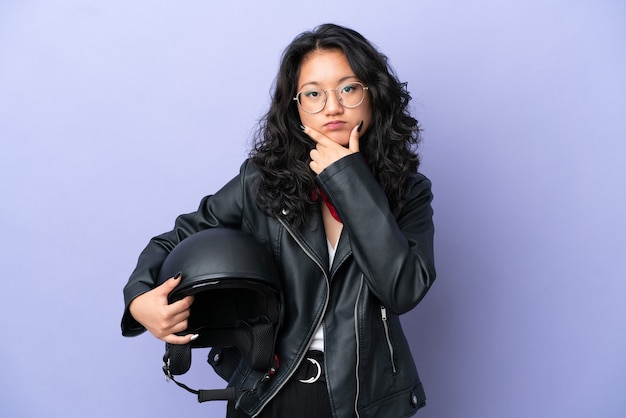 Młoda azjatycka kobieta z kaskiem motocyklowym na fioletowym tle myślenia