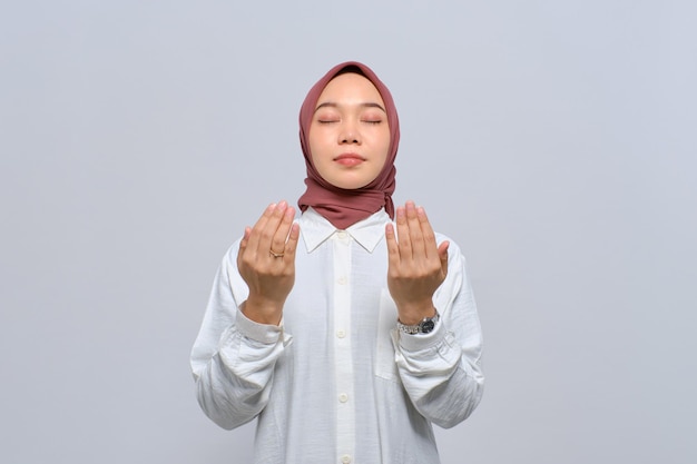 Młoda azjatycka muzułmanka podnosząca ręce i modląca się do boga odizolowanego na białym tle