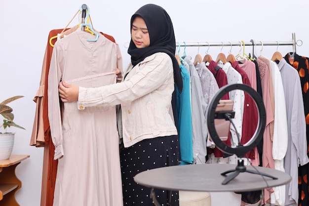 Młoda azjatycka muzułmanka sprzedająca ubrania online w mediach społecznościowych, mierzy rozmiar beig