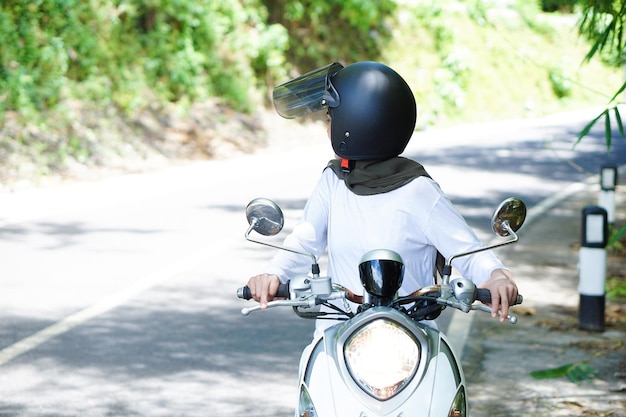 Młoda azjatycka muzułmańska kobieta jadąca motocyklem w kasku