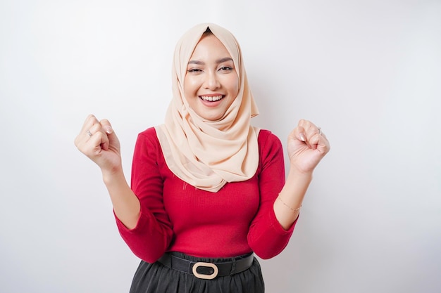 Młoda azjatycka muzułmańska kobieta z szczęśliwym, pomyślnym wyrazem twarzy, ubrana w hidżab odizolowany białym tłem