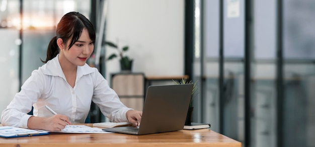 Młoda azjatycka piękna i urocza bizneswoman uśmiecha się i pracuje na laptopie w biurze