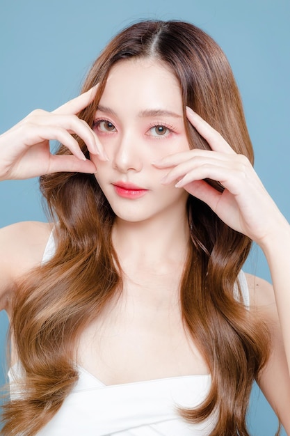Młoda azjatycka piękna kobieta kręcone długie włosy z koreańskim stylem makijażu na twarzy i idealnie czystą skórą na izolowanym niebieskim tle Zabiegi na twarz Kosmetologia Chirurgia plastyczna
