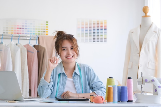 Młoda azjatycka projektantka mody siedzi przy biurku w studiu projektowym