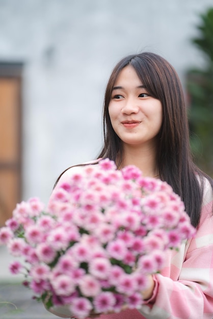 Młoda azjatycka śliczna dziewczyna ubrana w różową koszulę i trzymająca piękny różowy kwiat portret modelki z koncepcją natury z różowym kwiatem w ręku szczęśliwa i uśmiechnięta na zewnątrz