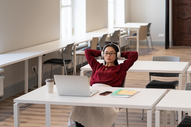 Młoda Azjatycka Studentka Nosząca Słuchawki, Studiująca Online W Czytelni Biblioteki