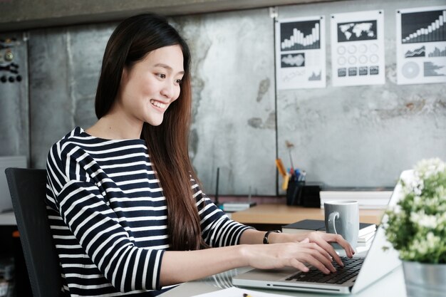 Młoda azjatykcia biurowa kobieta pracuje z laptopem przy biurka biura tłem