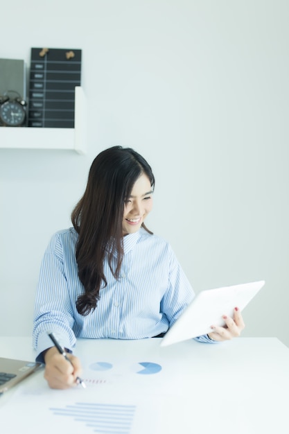 Młoda azjatykcia biznesowa kobieta używa pastylkę dla pracować przy biurkiem w biurze z dokumentami i laptopem.