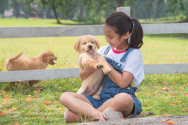 Młoda azjatykcia dziewczyna trzyma troszkę golden retriever psa w parku