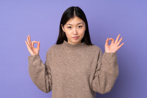 Młoda azjatykcia kobieta na purpury ścianie w zen pozie