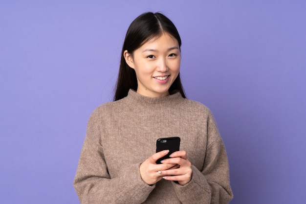 Młoda azjatykcia kobieta na purpury ścianie wysyła wiadomość z wiszącą ozdobą