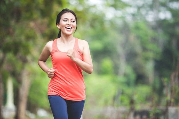 Młoda azjatykcia kobieta robi ćwiczeniu plenerowemu w parku, jogging