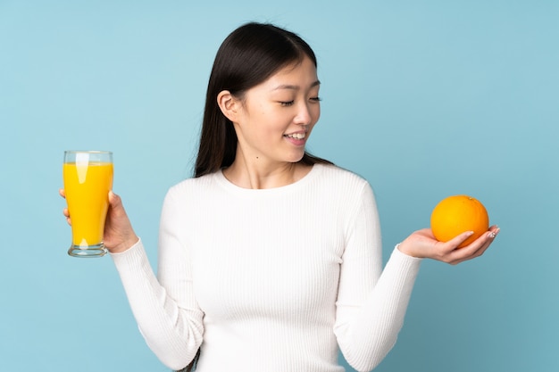 Młoda azjatykcia kobieta trzyma pomarańcze nad błękit ścianą
