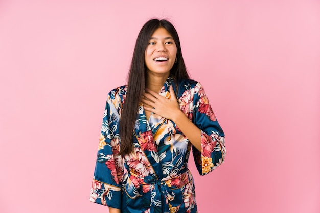 Młoda Azjatykcia Kobieta W Piżamie Kimono śmieje Się Głośno, Trzymając Rękę Na Piersi.