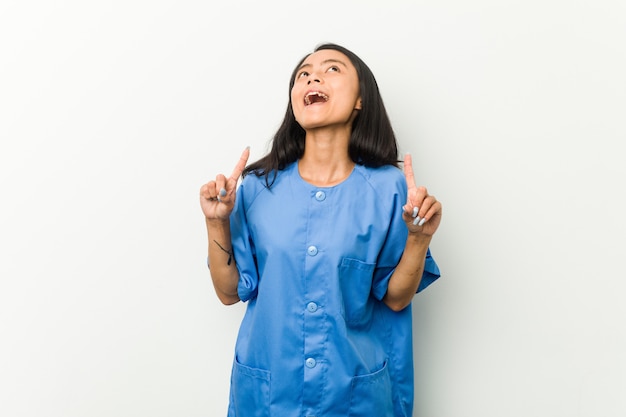 Młoda azjatykcia pielęgniarki kobieta wskazuje do góry z rozpieczętowanym usta.