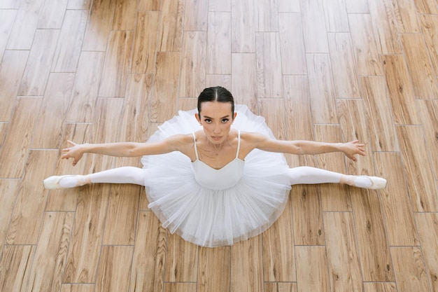 Młoda balerina w białym paczku pozuje na tle drewnianej podłogi