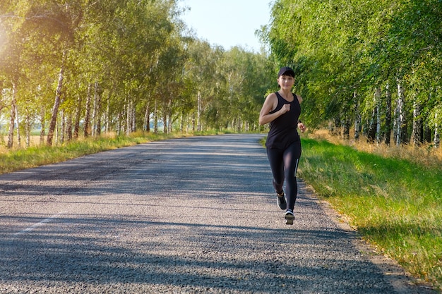 Młoda biała fitness kobieta biegnie wzdłuż wiejskiej drogi