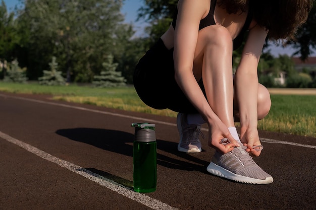Młoda biegaczka wiąże sznurowadła butelkę wody stoi w pobliżu zdrowy styl życia