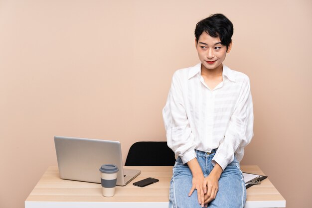 Młoda biznesowa Azjatycka kobieta w jej miejscu pracy stoi i patrzeje z boku