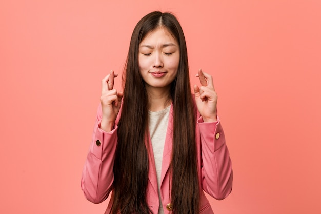 Młoda biznesowa Chińska kobieta jest ubranym różowego kostiumu skrzyżowanie dotyka dla mieć szczęście