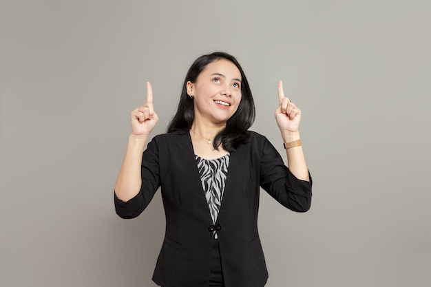 Młoda biznesowa kobieta nosi czarny garnitur, patrząc w górę i wskazując w górę dwiema rękami