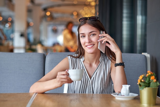 Młoda biznesowa kobieta opowiada na telefonie w sklep z kawą