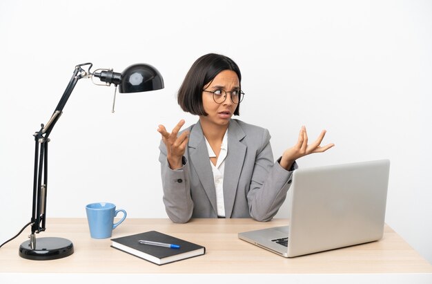 Młoda biznesowa kobieta rasy mieszanej pracująca w biurze z wyrazem zaskoczenia, patrząc z boku