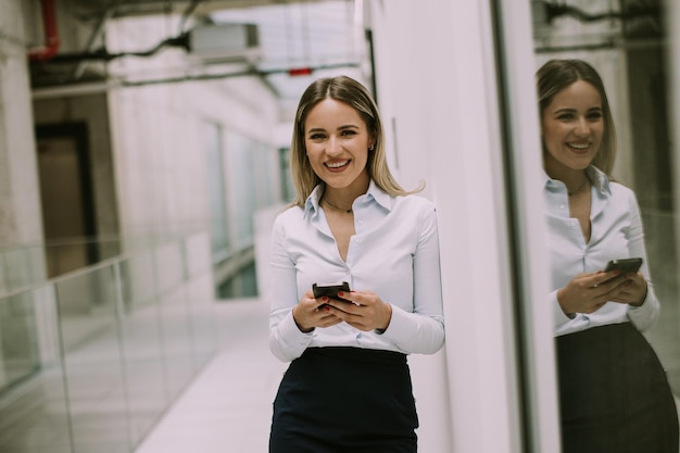 Młoda biznesowa kobieta używa telefon komórkowego w biurowym korytarzu