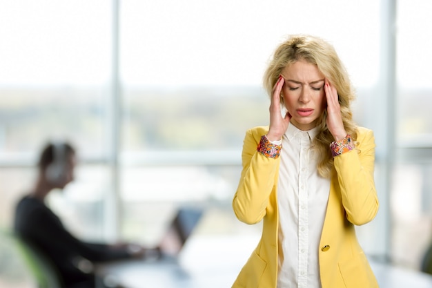 Zdjęcie młoda biznesowa kobieta z okropnym bólem głowy. przygnębiona młoda menedżerka dotykająca jej kości policzkowej i mająca zamknięte oczy, stojąc przed oknem biura.