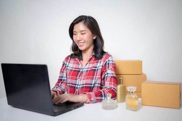 Młoda bizneswoman azjatycka pakuje produkty w paczkę zgodnie z zamówieniem klienta