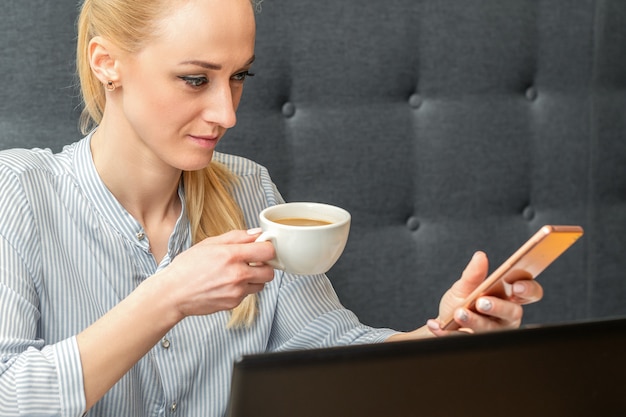 Młoda bizneswoman kaukaski z smartphone i filiżankę kawy, pracująca w domowym biurze