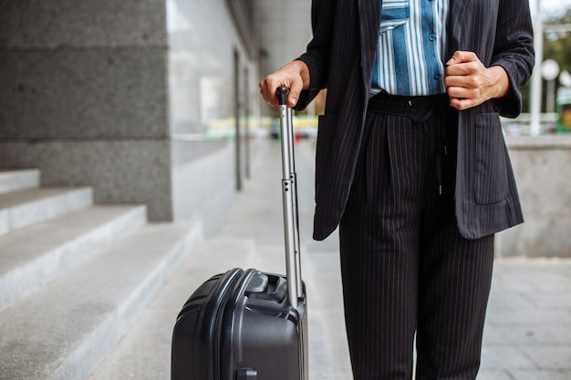 Młoda bizneswoman stoi z walizką w pobliżu hotelu i czeka na taksówkę