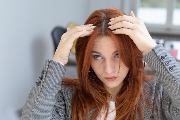 Zdjęcie młoda bizneswoman z farbowanymi rudymi włosami sprawdza w lustrze odrost korzeni