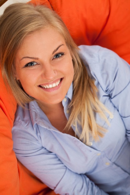 Zdjęcie młoda blond kaukaska uśmiechająca się na pomarańczowej kanapie.