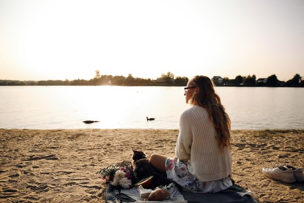 Młoda blond kobieta dziewczyna leżąc na plaży wiosną w biały sweter z dzianiny ze szkockim kotem w słoneczny dzień na pikniku