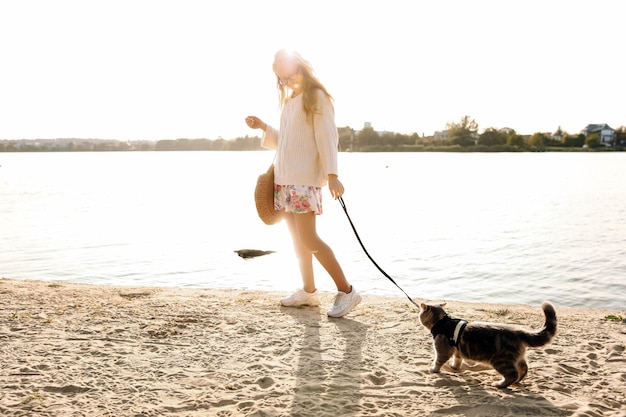 Młoda blond kobieta dziewczyna spaceru na plaży wiosną w sukience i białym swetrze z kotem na a