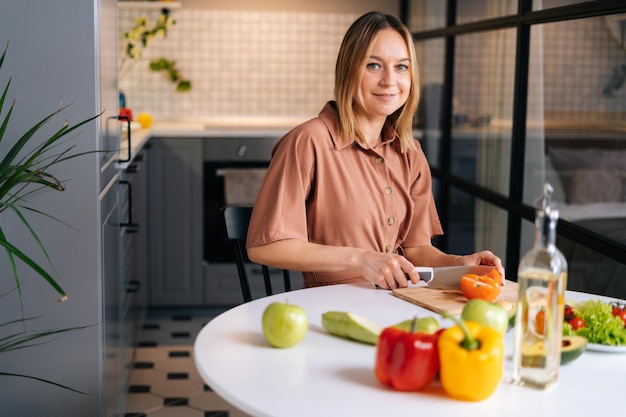 Młoda blond kobieta kroi cebulę w kuchni z nowoczesnym wnętrzem patrząc na kamery Pojęcie zdrowego odżywiania