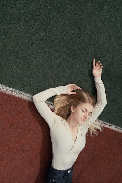 Młoda blond kobieta leżąca na boisku backetball z zamkniętymi oczami selektywna ostrość