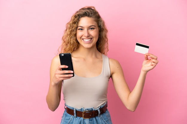 Młoda blond kobieta odizolowana na różowym tle kupując za pomocą telefonu komórkowego za pomocą karty kredytowej